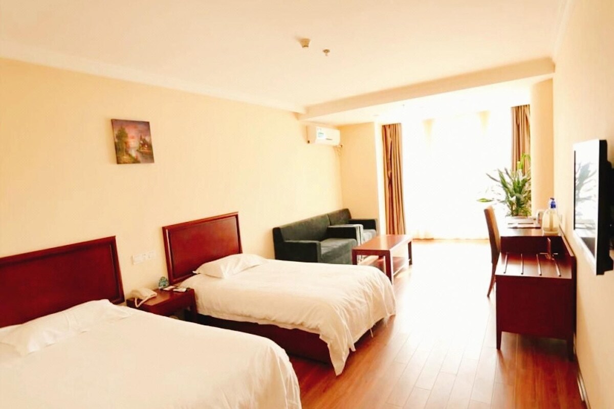Hotellihuone, jossa on kaksi sänkyä, työpöytä, tuoli, televisio ja ikkuna, jossa on verhot.