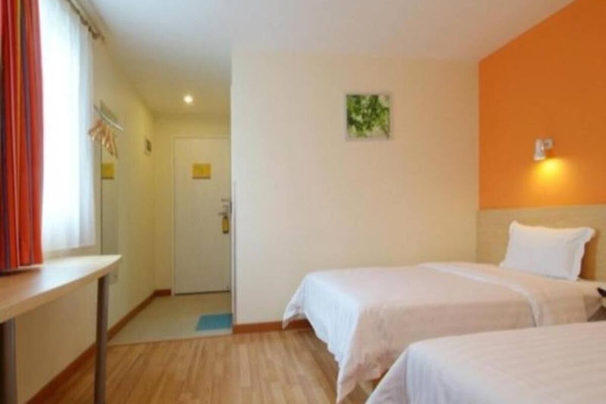 Habitación de hotel con dos camas, un escritorio, una puerta y una lámpara pequeña de pared.