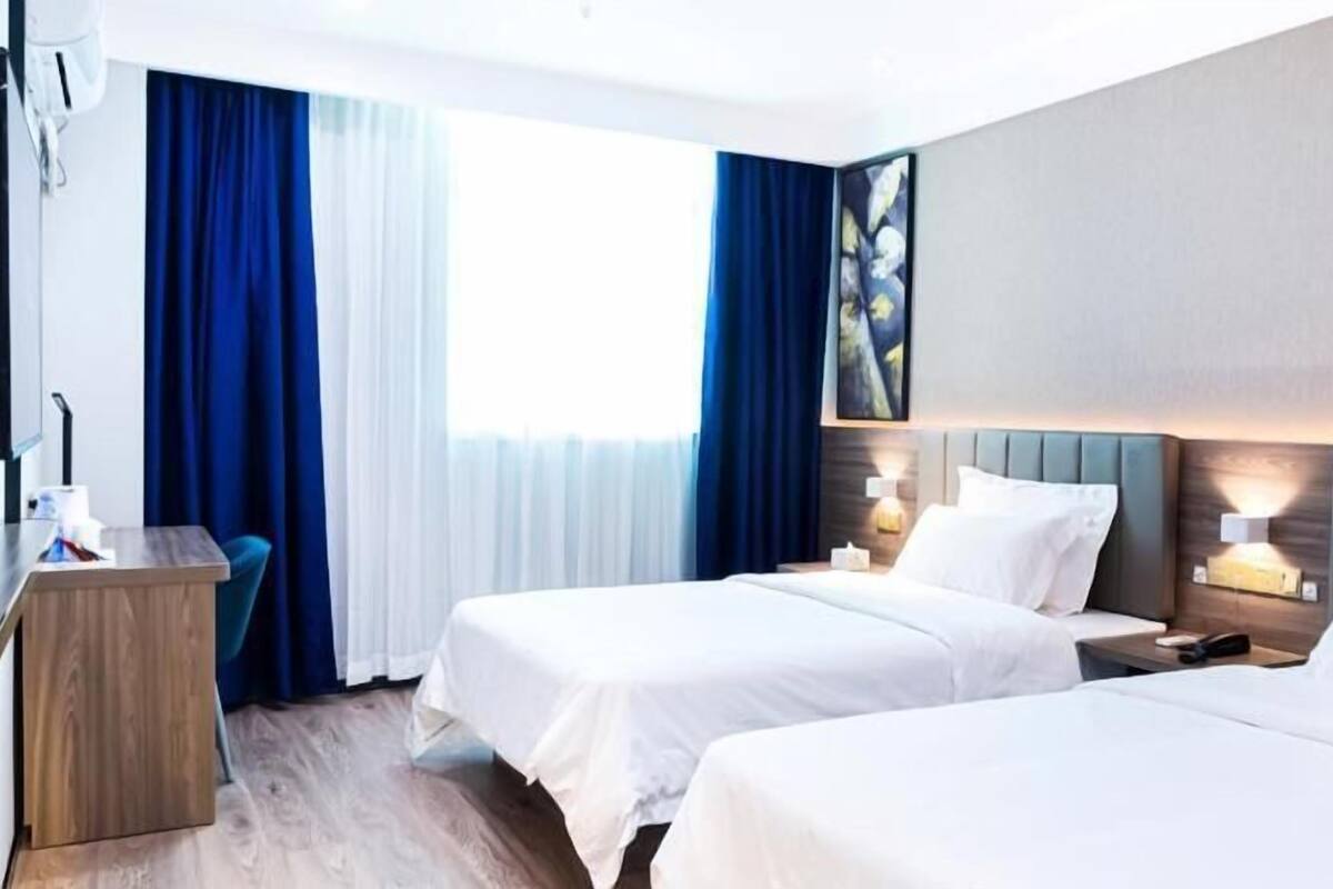 Habitación de hotel con dos camas, un escritorio y un ventanal con cortinas.