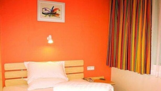 A hotel room with a bed, a wall-mounted light, a framed picture, and a window with colorful curtains. - 7 Days Inn Tangshan Haigang District Haicheng Road (Tangshan)