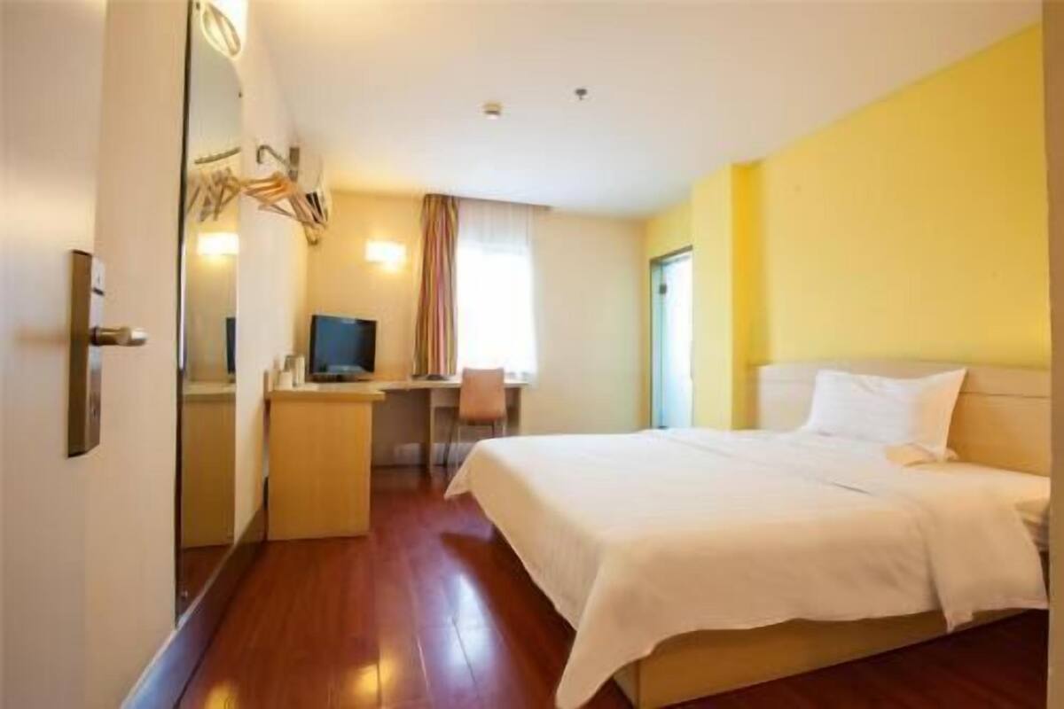 Una habitación de hotel con cama, escritorio, computadora, espejo y puerta.
