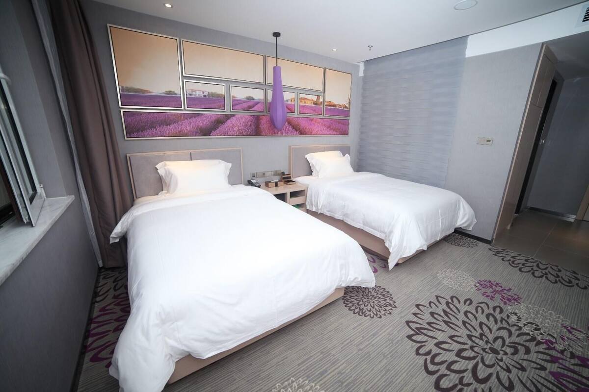 Ein Hotelzimmer mit zwei Betten, einem großen Fenster mit Blick auf Lavendelfelder, einer modernen Pendelleuchte und einem gemusterten Teppich.