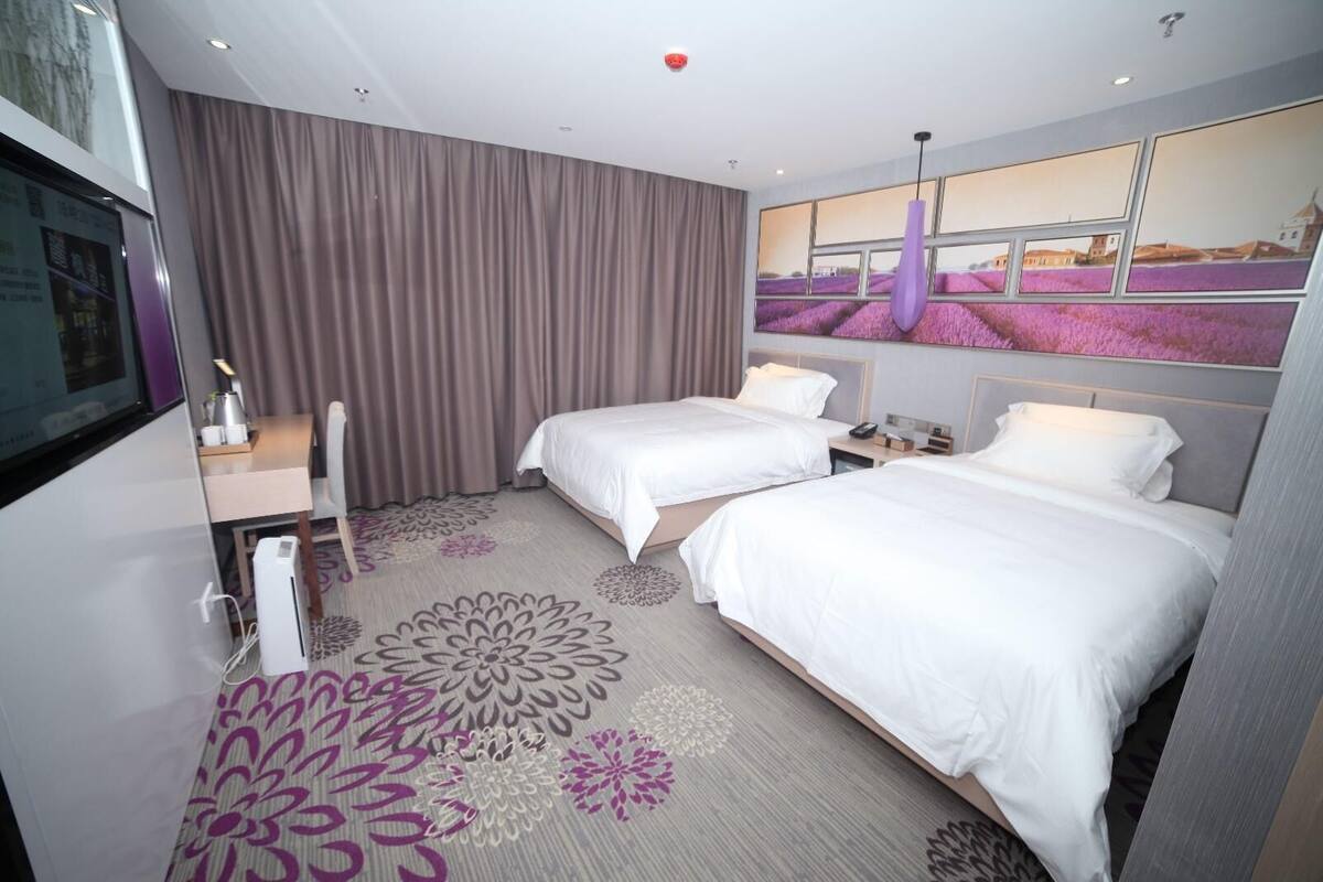 Ein Hotelzimmer mit zwei Betten, einem Schreibtisch, einem Stuhl, einem Fernseher und einem großen Fenster mit Blick auf Blumen.