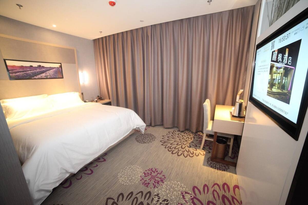 Ein Hotelzimmer mit Bett, Schreibtisch mit Stuhl, großem Spiegel, Wand-Fernseher und einem Fenster mit Vorhängen.