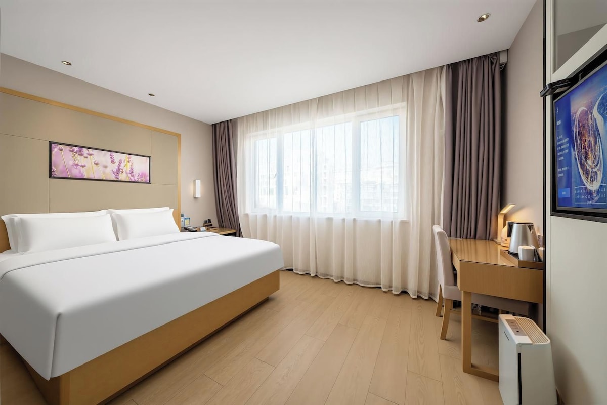 Ein Hotelzimmer mit einem Bett, einem Schreibtisch, einem Stuhl, einem Flachbildfernseher und einem Fenster mit Vorhängen.