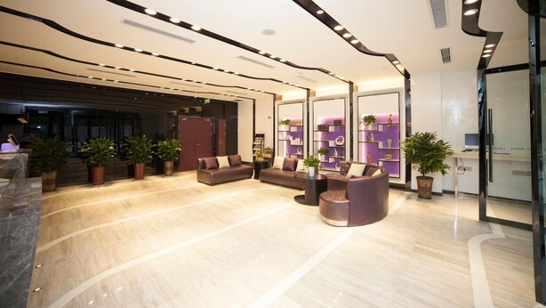 Um lobby moderno com teto curvo, assentos confortáveis, plantas em vasos e um balcão de atendimento.