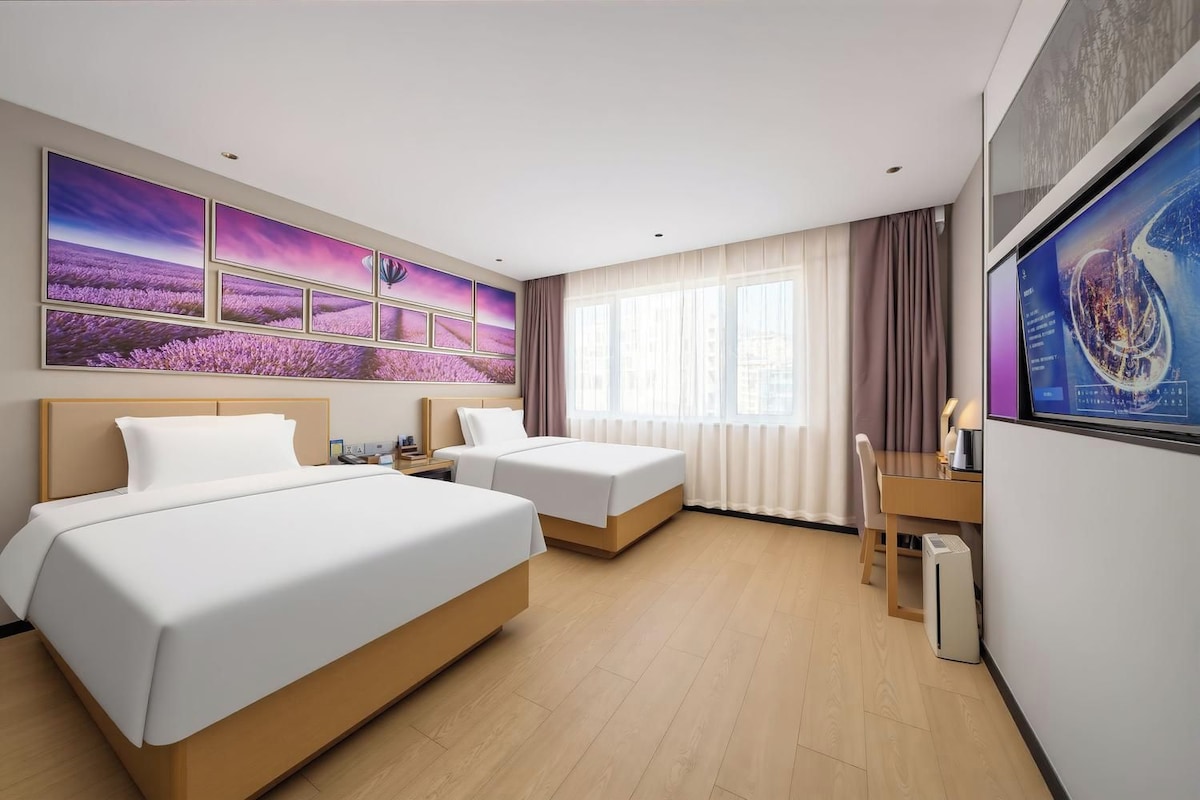 Ein Hotelzimmer mit zwei Betten, einem Schreibtisch und einem großen Fenster mit Vorhängen.