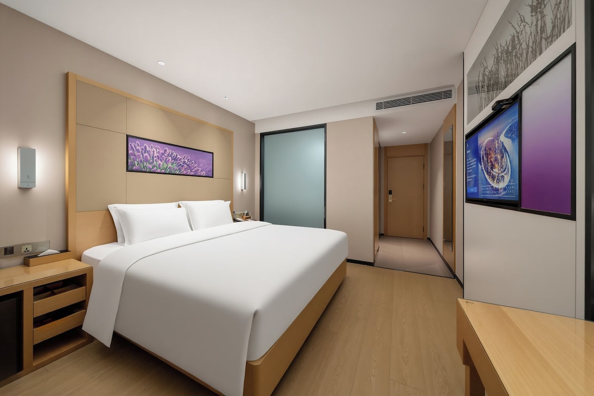 Ein modernes Hotelzimmer mit einem großen Bett, Nachttischen, einem Schreibtisch und einem großen Fenster.
