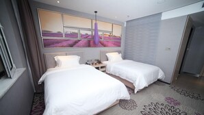 Quarto de hotel com duas camas, uma janela grande com vista para campos de lavanda, uma luminária pendente moderna e um tapete estampado.