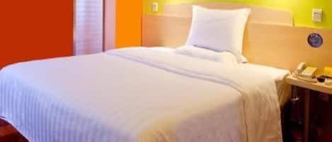 Una habitación de hotel con una cama, una mesita de noche con teléfono y una lámpara fijada a la pared.