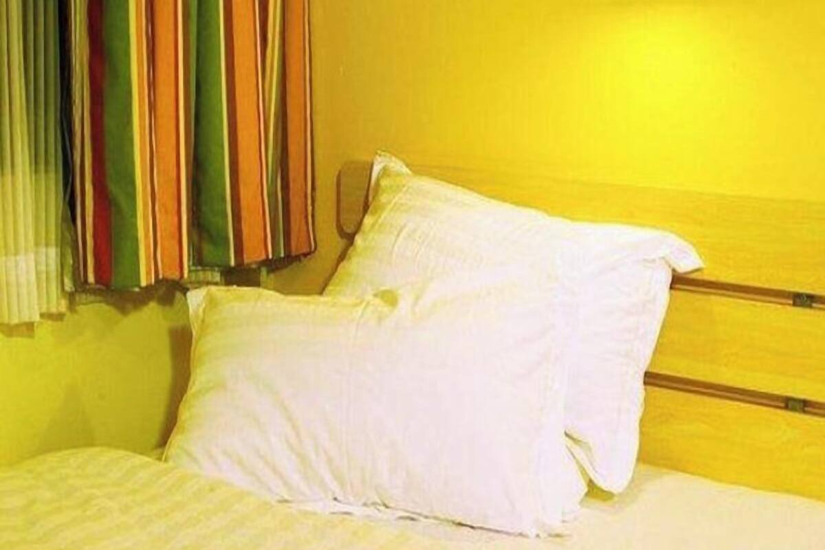 Una cama con ropa de cama blanca, cabecera de madera y cortina a rayas.