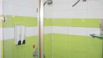 A bathroom with green and white tiles, a glass shower enclosure, and a hand dryer.