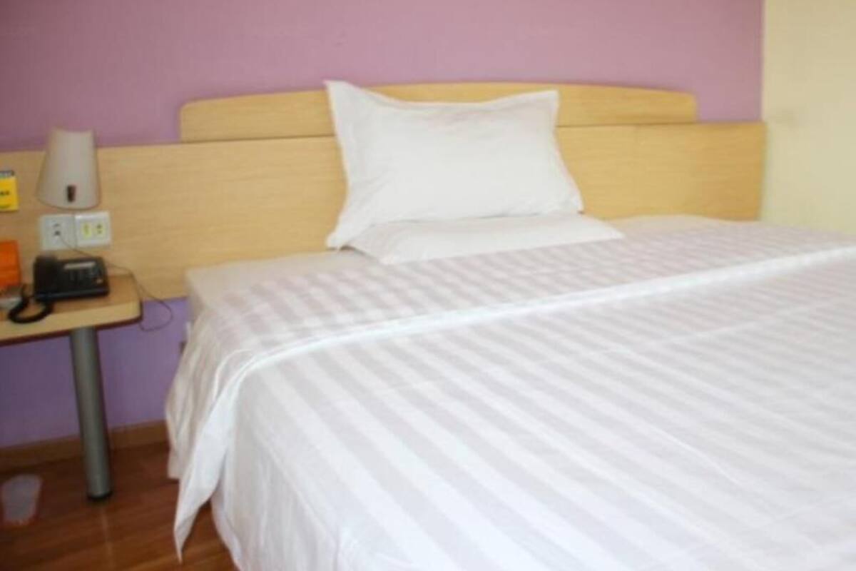 A single bed with a wooden headboard, a bedside table with a lamp, and a power outlet.