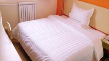 A single-bed room with a white bedspread, a nightstand, a chair, and a radiator.