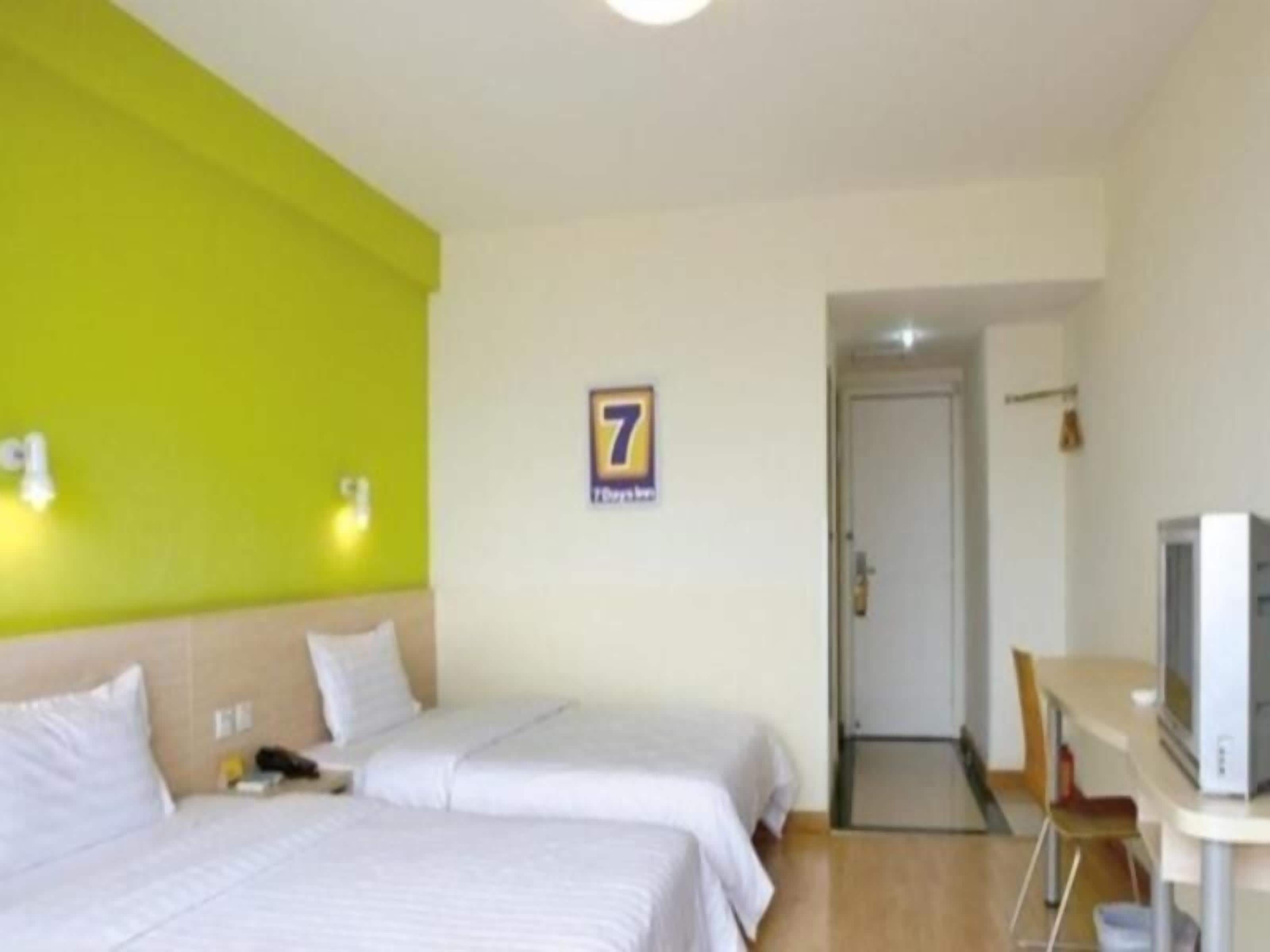 A hotel room with two beds, a desk with a television, and a door leading to another room.