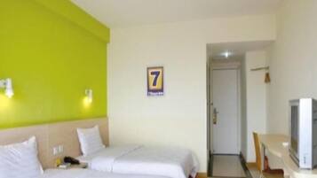 A hotel room with two beds, a desk with a television, and a door leading to another room.