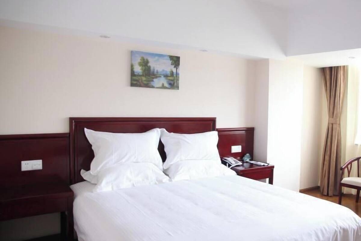 A hotel room with a large bed, a nightstand, a telephone, and a painting on the wall.