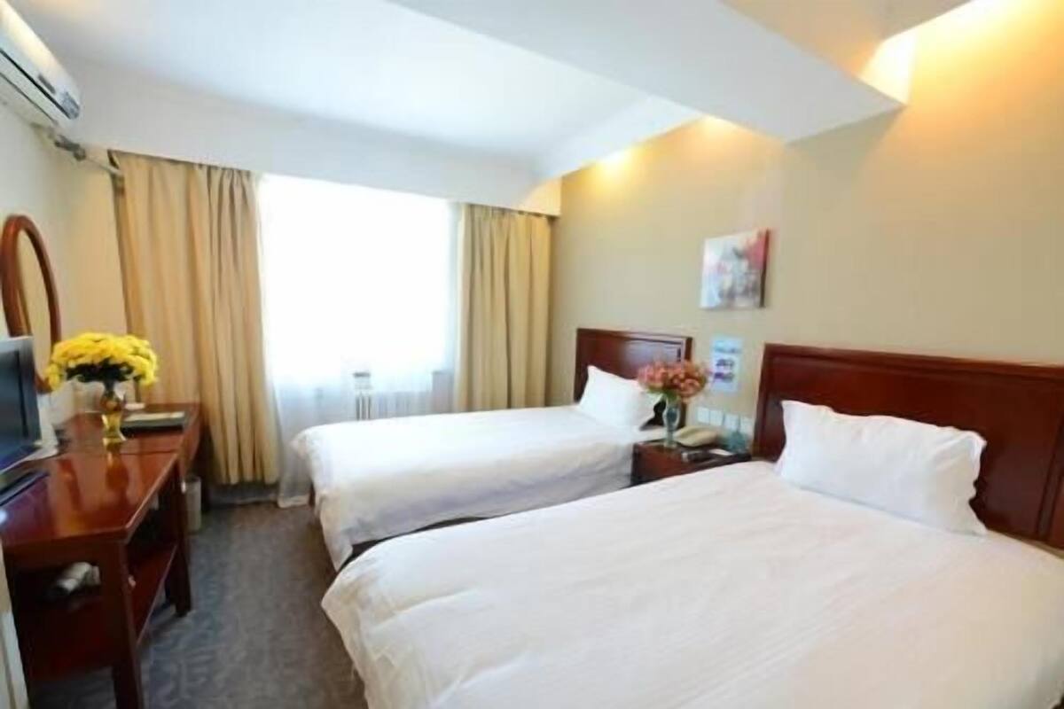 A hotel room with two beds, a desk, a chair, a TV, and a window with curtains.