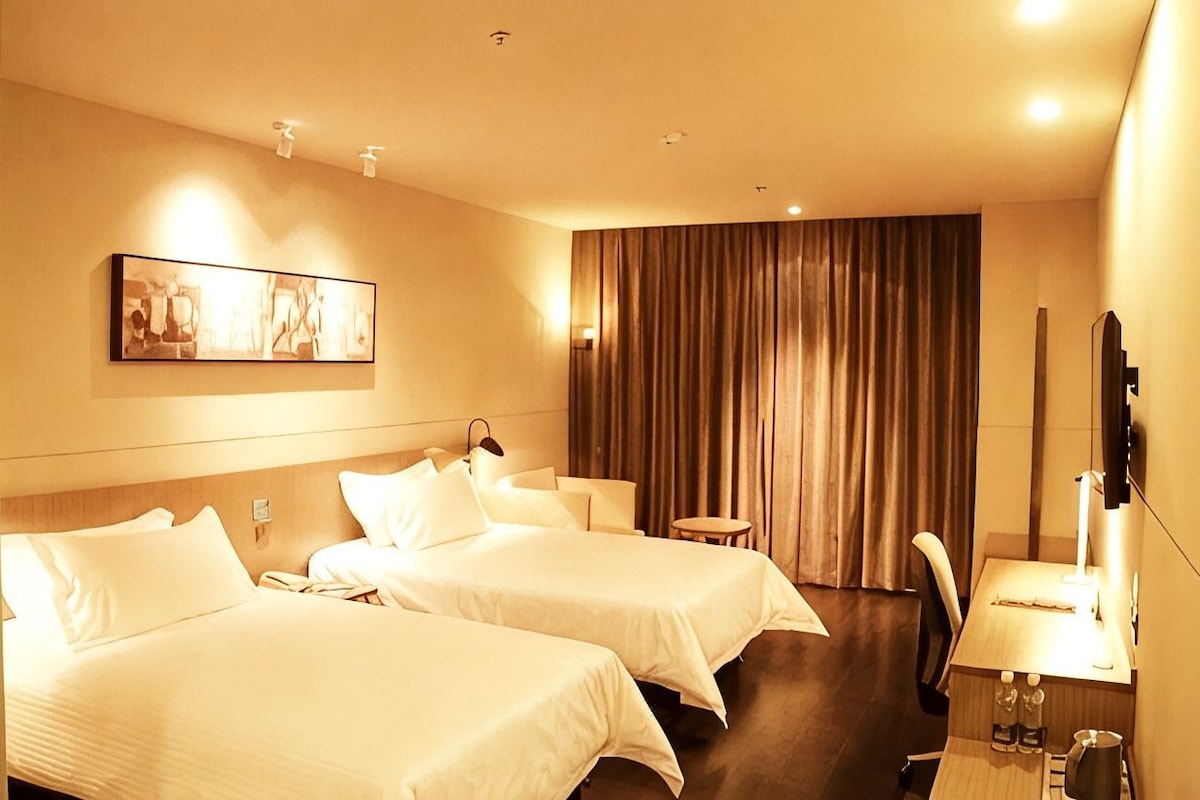 Habitación de hotel con dos camas, un escritorio con silla, un televisor y un cuadro en la pared.
