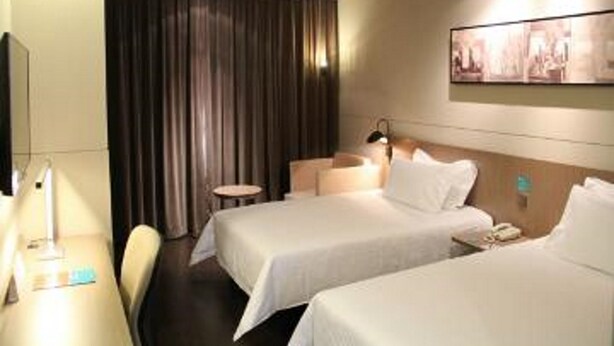 A hotel room with two beds, a desk, a chair, a small table, a wall-mounted TV, and a curtain. - Jinjiang Inn Select (Shenyang)
