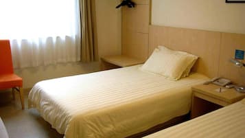 A hotel room with two beds, a chair, a bedside table with a phone, and a coat rack.