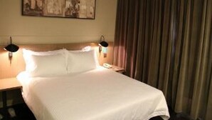 A hotel room with a bed, nightstand, lamp, and a painting on the wall. - Jinjiang Inn Select (Shenyang)