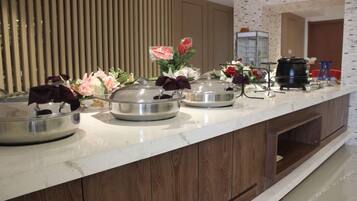 A buffet setup with multiple serving stations, a coffee machine, and decorative flowers.