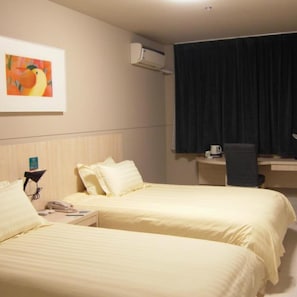 Habitación de hotel con dos camas, un escritorio, una silla, un equipo de aire acondicionado y un cuadro en la pared.