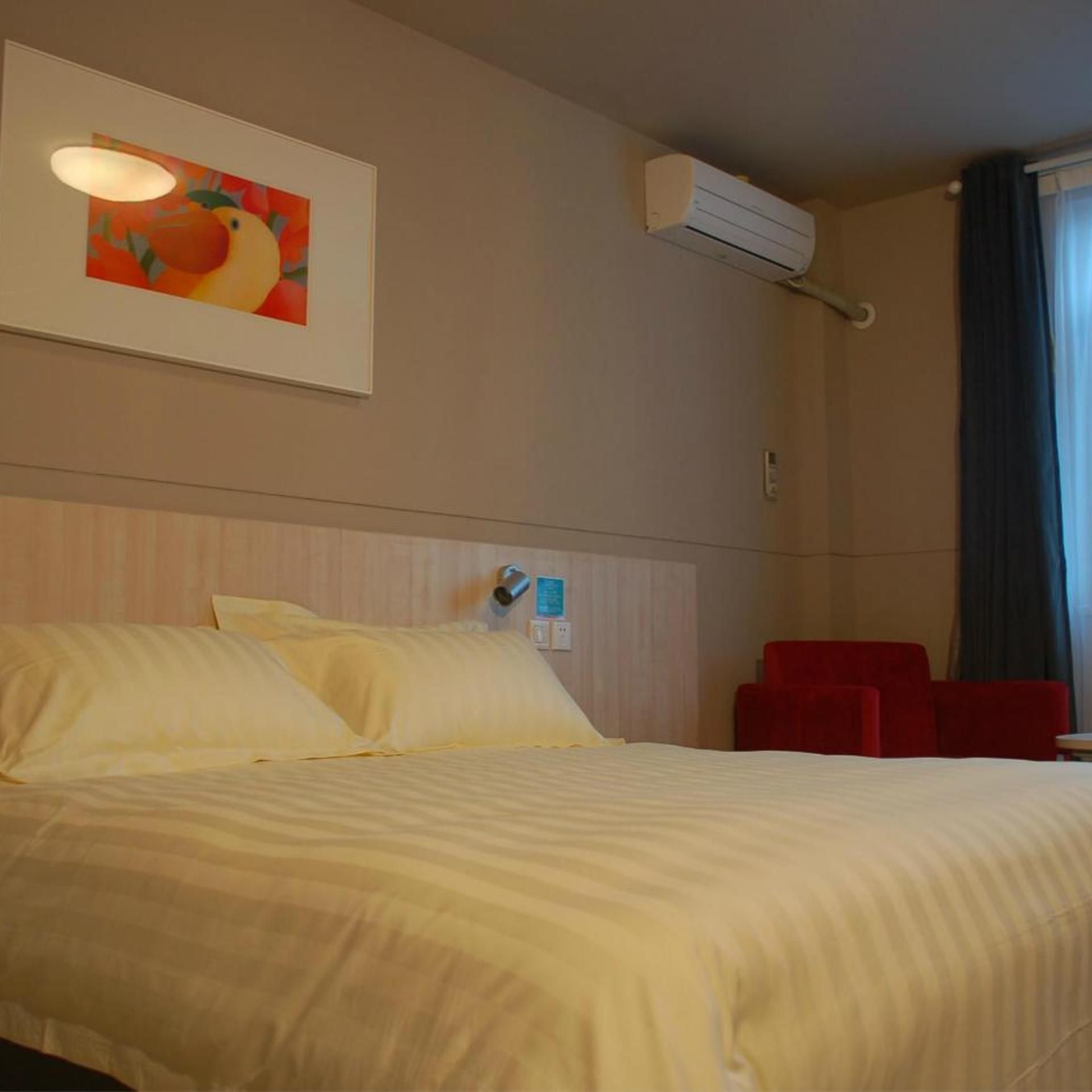 Une chambre d’hôtel avec un lit, une chaise rouge, un appareil de climatisation et un tableau accroché au mur.