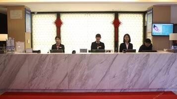 A reception desk with four staff members seated behind it, a red carpet, and a television screen on the wall.