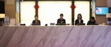 A reception desk with four staff members seated behind it, a red carpet, and a television screen on the wall.