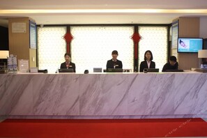 A reception desk with four staff members seated behind it, a red carpet, and a television screen on the wall. - Jinjiang Inn Select (Shenyang)