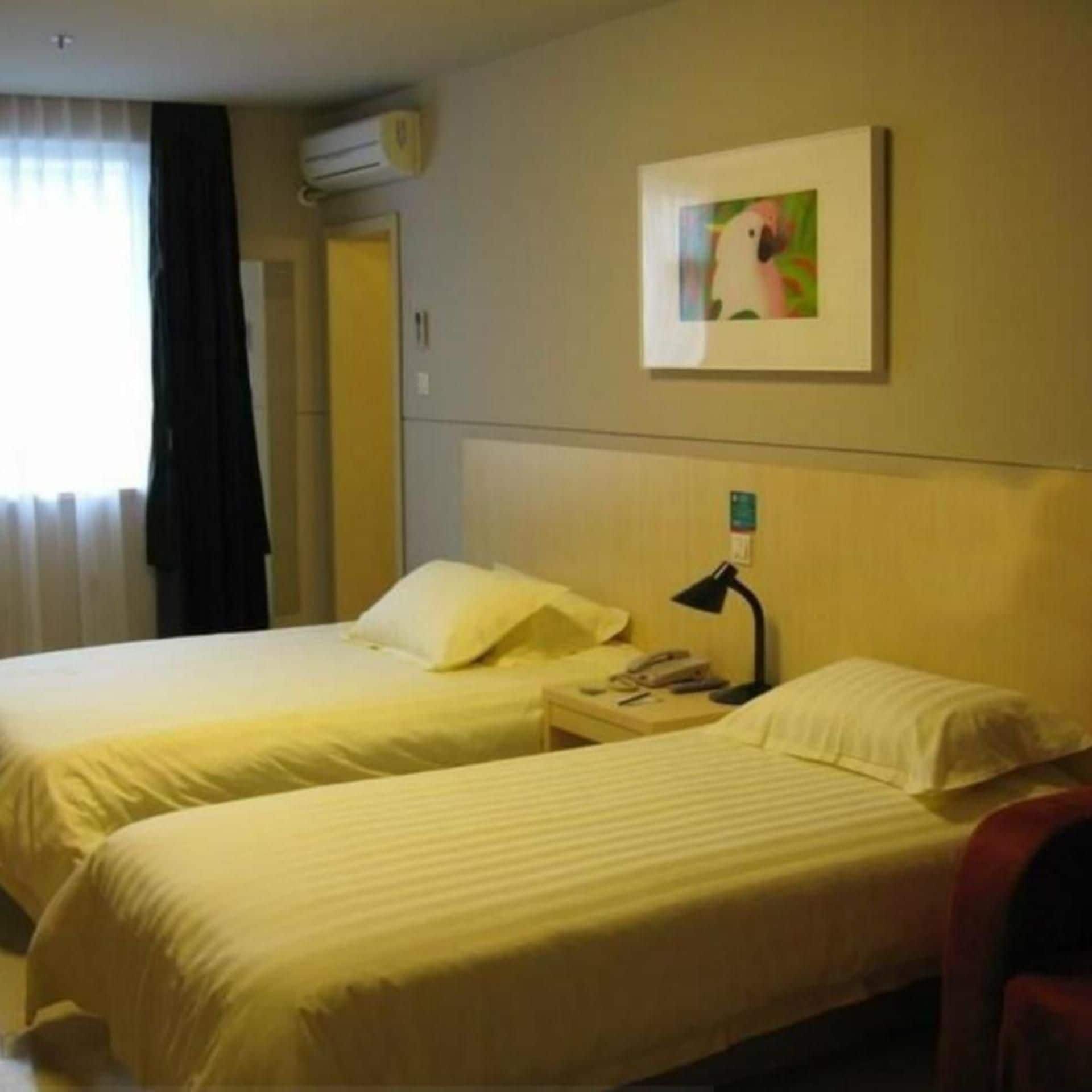 A hotel room with two beds, a nightstand with a lamp, and a painting on the wall.
