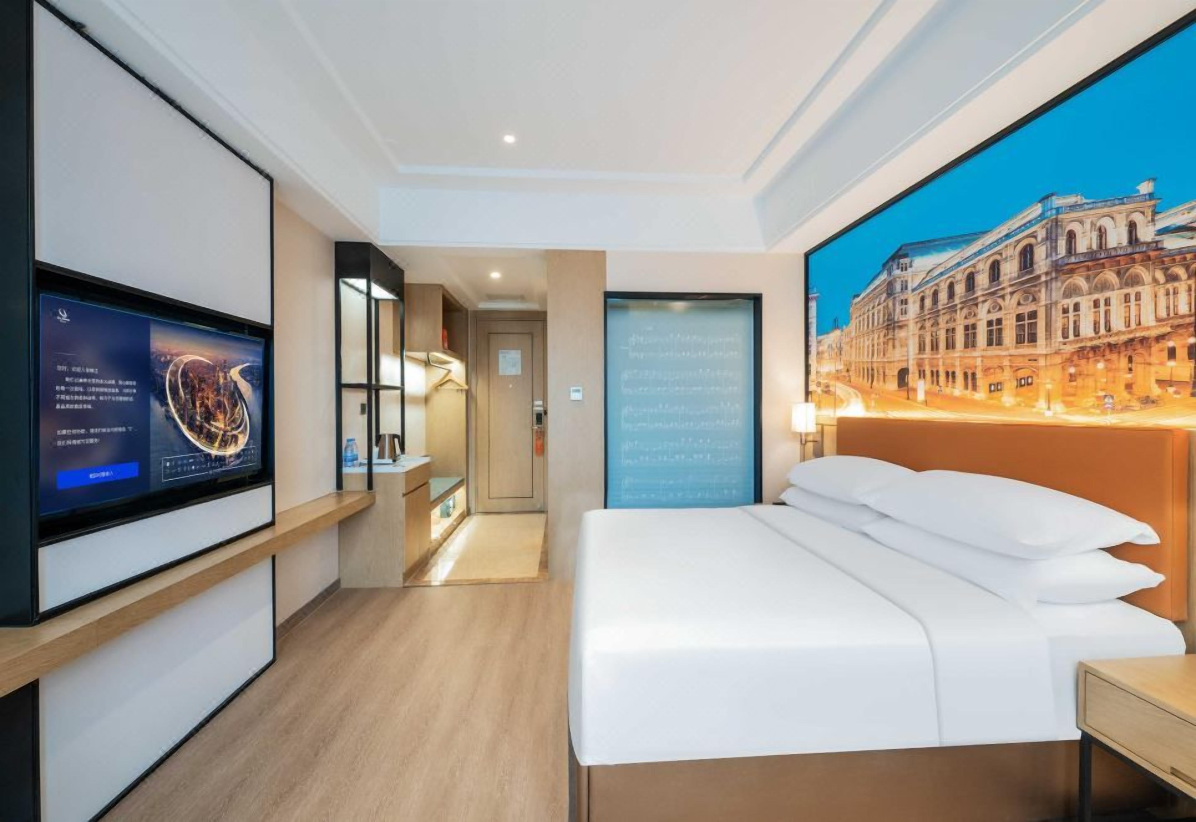 A hotel room with a bed, a TV, a chalkboard, and a large window with a cityscape view.