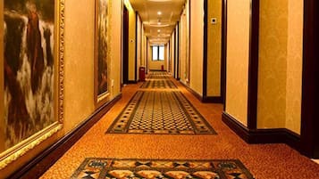 Un largo y estrecho pasillo de hotel con alfombra estampada, obras de arte enmarcadas en las paredes y un diseño simétrico.