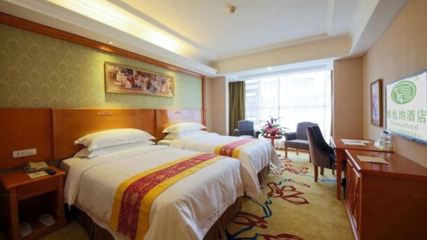 A hotel room with two beds, a desk, a chair, a small table with a vase, and a window with curtains. - Vienna International Hotel (Lhasa)