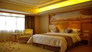 A hotel room with a large bed, a chair, a nightstand, and a painting on the wall. - Vienna International Hotel (Lhasa)