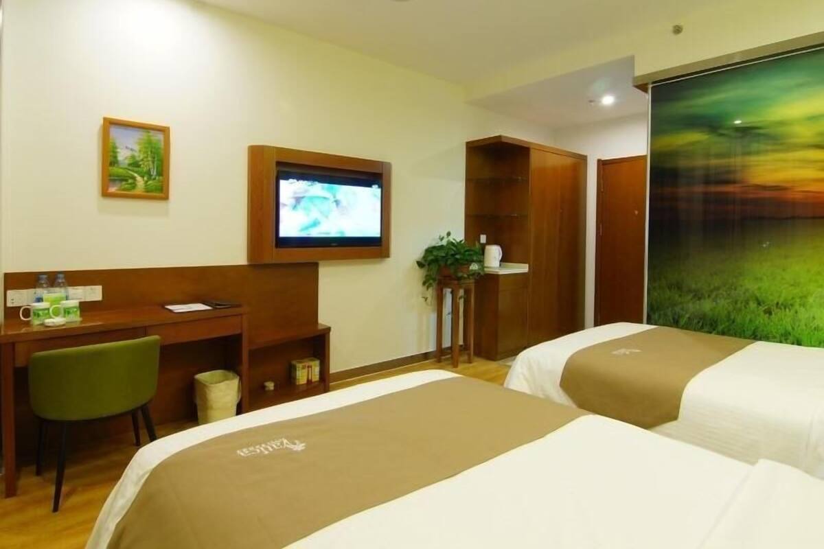 Ein Hotelzimmer mit zwei Betten, einem Schreibtisch, einem Fernseher und einem großen Fenster mit Blick.