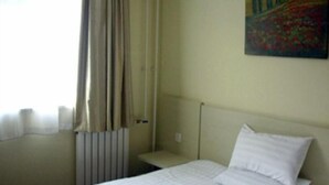 Et hotelværelse med en seng, en radiator, et vindue med gardiner og et maleri på væggen.