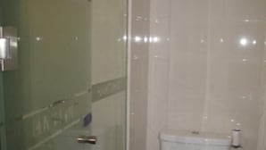 Et badeværelse med glasvæg omkring brusebad, toilet og et vandhanefæste på væggen.