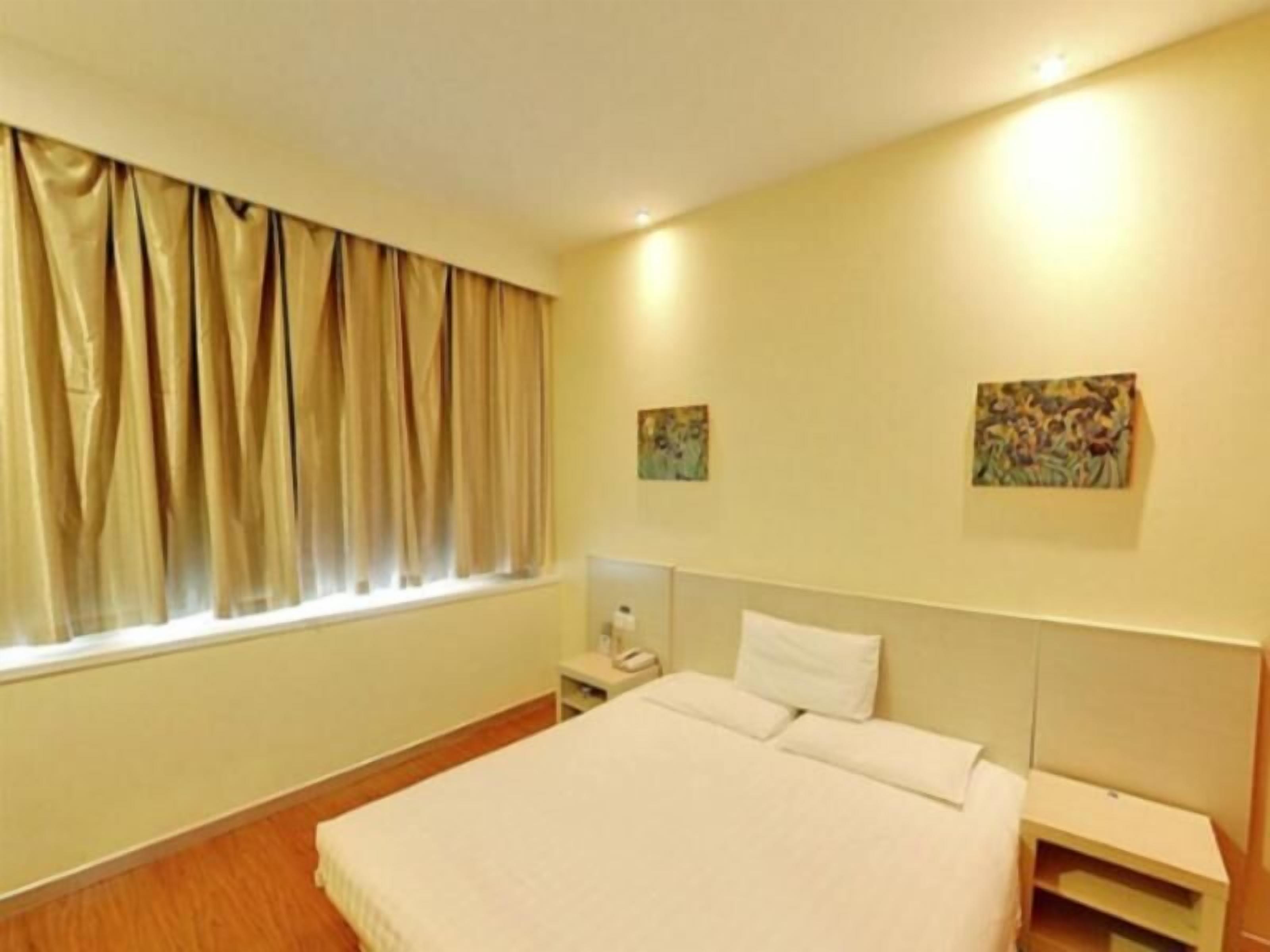 Habitación de hotel con cama, mesita de noche, ventana con cortinas y dos cuadros colgados en la pared.