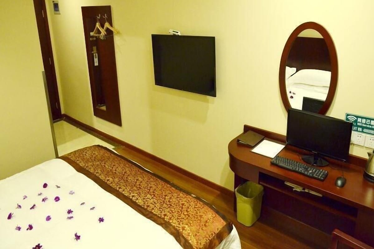 Quarto de hotel com cama, escrivaninha com computador, televisão, espelho e porta.