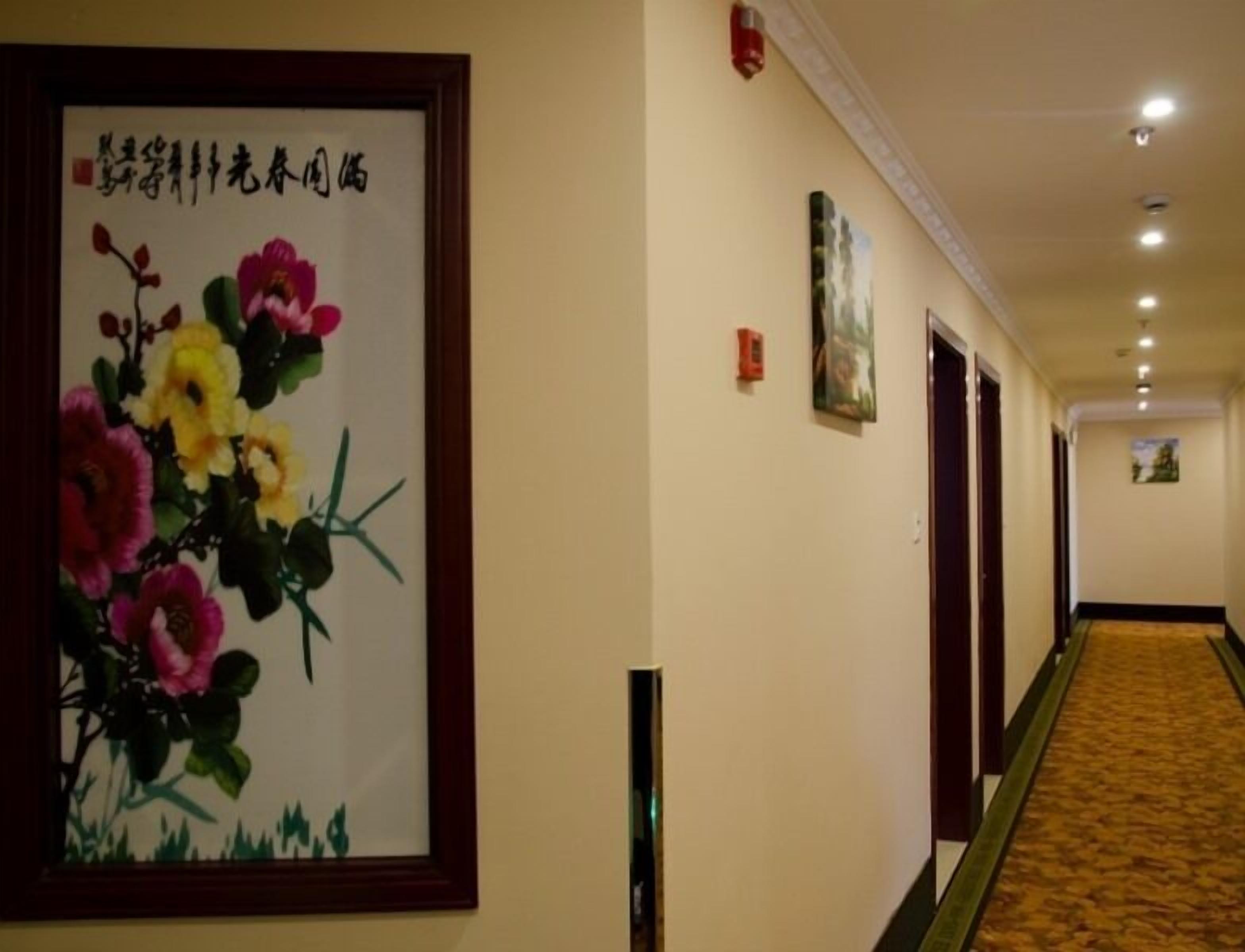 A hotel hallway with a framed floral artwork on the left, a carpeted floor, and doors on the right.