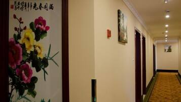A hotel hallway with a framed floral artwork on the left, a carpeted floor, and doors on the right.