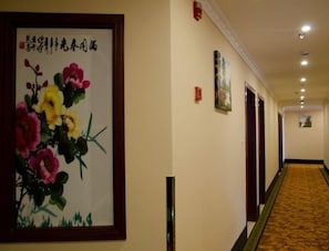 A hotel hallway with a framed floral artwork on the left, a carpeted floor, and doors on the right. - Greentree Inn (Shanghai)