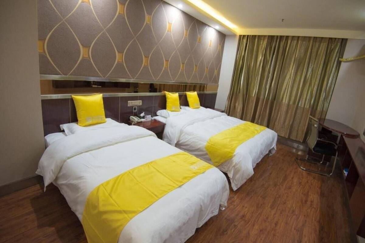 A hotel room with two beds, a wooden floor, a modern headboard, and a curtain.