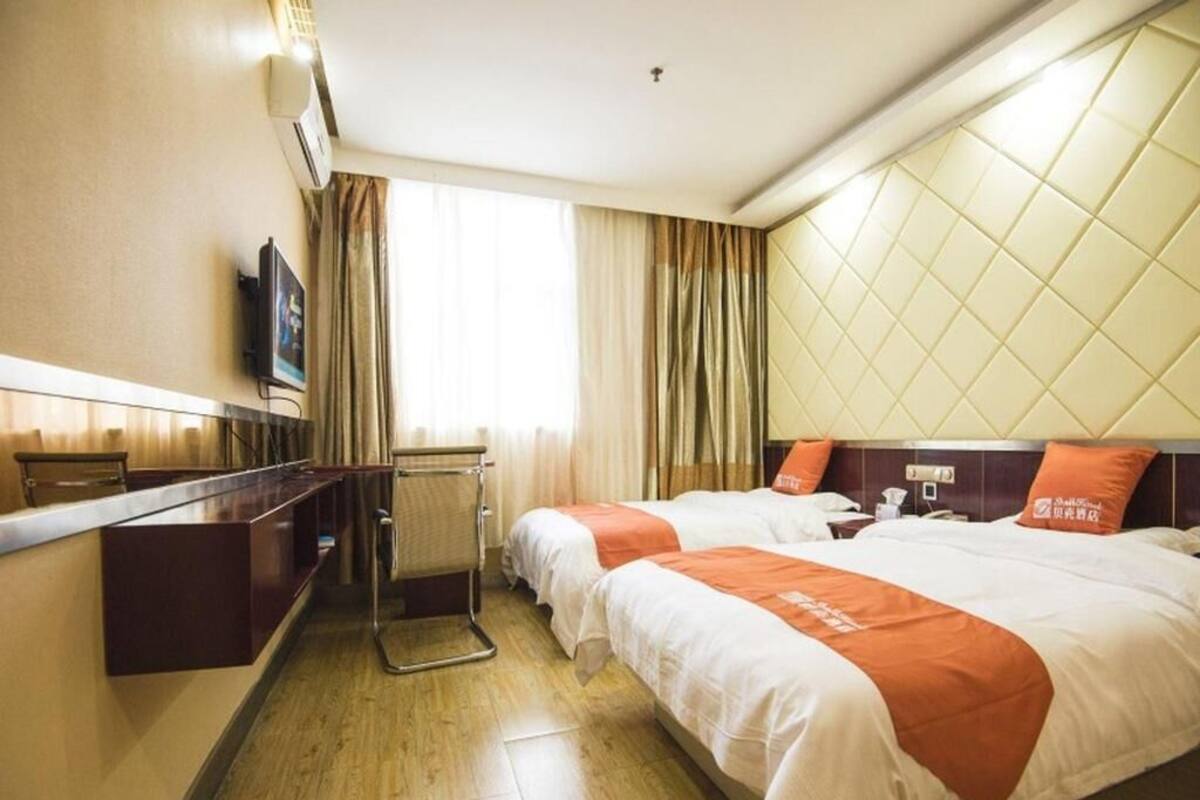 A hotel room with two beds, a desk, a television, and a window with curtains.
