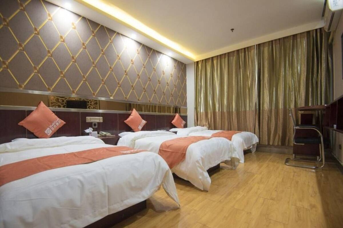 A hotel room with four beds, a wooden floor, a patterned wall, and a curtain.