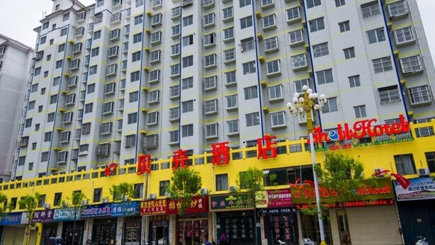 A multi-story hotel with a yellow facade, multiple balconies, and various storefronts on the ground level. - Shell Hotel (Dingxi)