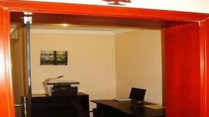 Ein Zimmer mit Schreibtisch, Stuhl und Computer. Eine Tür mit Griff und einem kleinen Schild darüber.
